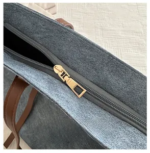 Dettaglio della cerniera dorata e del manico in pelle marrone sulla borsa blu in tessuto