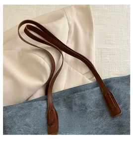 Dettaglio di borsa tote in pelle scamosciata blu con manici marroni e testo grafico