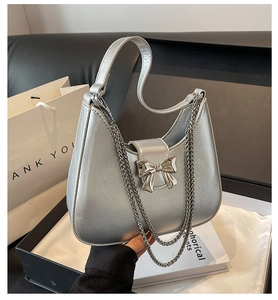 Silver metallic hobo crescent bag featuring a decorative bow buckle and chain detail