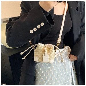 Close-up of beige woven straw mini bucket bag with white leather trim on model
