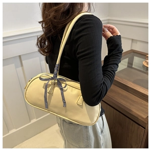 Detail view of cream yellow cylindrical shoulder bag with blue plaid ribbon on model