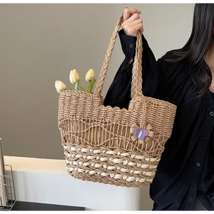 Détail d'un sac cabas en paille tressée avec pendentif papillon violet et tulipes blanches