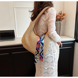 Detail of woven straw tote bag with brown leather handle and vibrant patterned silk scarf