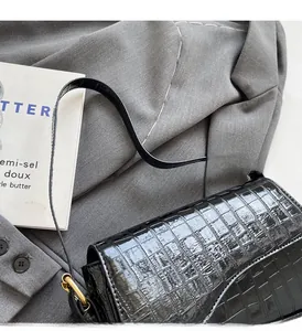 Detail of black glossy crocodile texture on the shoulder bag with golden hardware