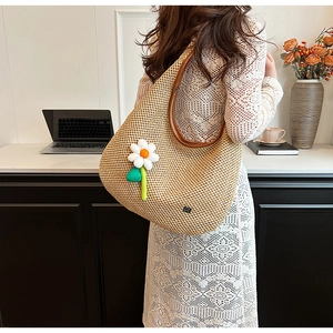 Detailed side view of beige straw hobo shoulder bag with daisy charm and leather handle