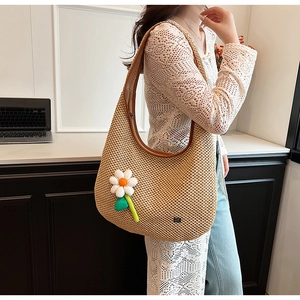 Detail of hand-made straw shoulder bag with daisy floral charm and half-moon hobo design