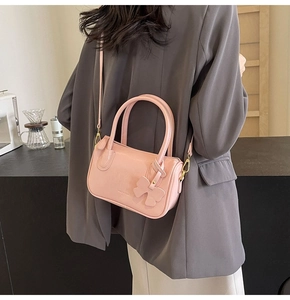 Detailed view of pink PU leather crossbody bag with bow charm and top handles