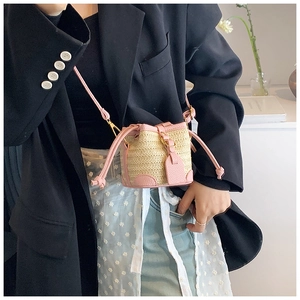 Detailed close-up of a mini straw bucket bag with pink leather trim and strap on a model