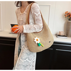 Detail of woven straw tote bag featuring white daisy charm and brown leather straps