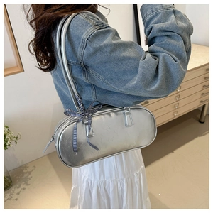 Detail of silver metallic cylinder bag featuring a side bow ribbon and long strap