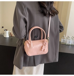 Pink glossy PU leather Boston bag with bow charm worn by a model in a grey suit