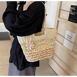Détail d'un sac en paille avec anses tressées et pendentif fleur papillon violet