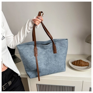Dettaglio della borsa tote in denim blu con manici in pelle marrone in ufficio minimal