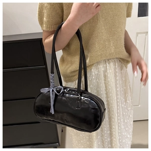 Close-up of black glossy patent leather shoulder bag with a stylish checkered ribbon bow