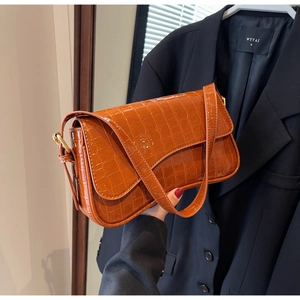 Detail of orange-brown croc-embossed underarm bag with glossy finish and gold metal buckle