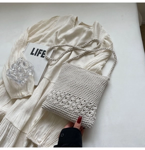Nahaufnahme der beigen handgewebten Stricktasche mit Blumenmuster auf weißem Kleid