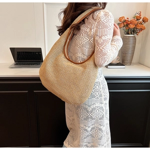 Detail view of woven straw tote bag with brown leather trim worn by model in an office