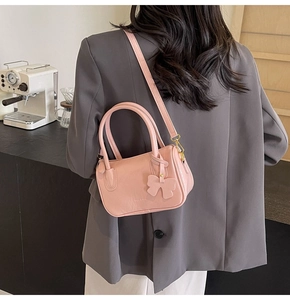 Pink PU leather crossbody bag with a cute bow charm shown on a model in a cozy cafe