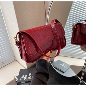 Detail of red crocodile pattern patent leather shoulder bag with gold metal buckle