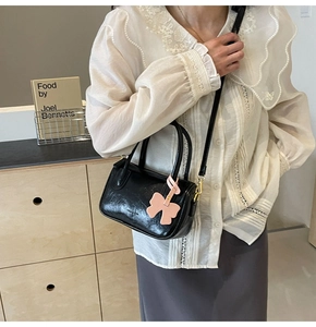 Detail of black glossy PU leather handbag featuring a pink leather bow charm and top handles