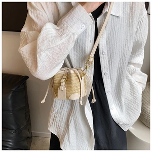 Detail of mini straw bucket bag with cream leather trim and drawstring closure on model