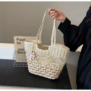 Gros plan détaillé du sac cabas en paille tressée avec contraste et breloque fleurie