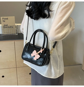 Detail of black glossy PU leather handbag with pink bow pendant and gold hardware details