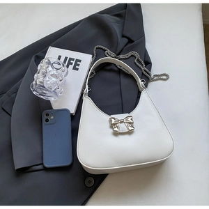 Close-up of a white crescent shoulder bag with a silver metal bow on a grey blazer