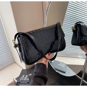 Detail shot of black crocodile embossed patent leather underarm bag with gold metal clasp