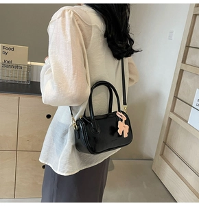 Detailed side view of black patent leather crossbody bag with pink bow charm on model