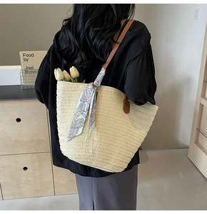 Detail of a beige woven straw tote bag with brown leather handles and a blue floral scarf