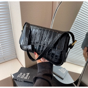 Detail of black crocodile texture baguette bag with glossy finish and gold metal buckle