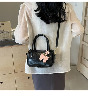 Fashionable black glossy PU crossbody bag worn by model with a pink bow charm detail