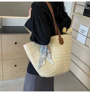 Detail of hand-woven straw tote bag with brown faux leather straps and floral scarf decor