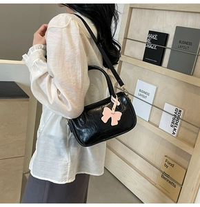 Black glossy PU handbag with a pink bow charm shown on a stylish wooden shelf display