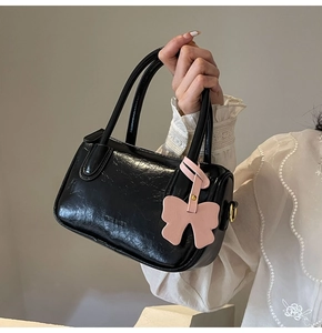Detail of black glossy pleated PU leather handbag with pink bow charm and gold-tone hardware