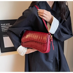 Deep red crocodile embossed leather underarm bag worn by a model in a black coat