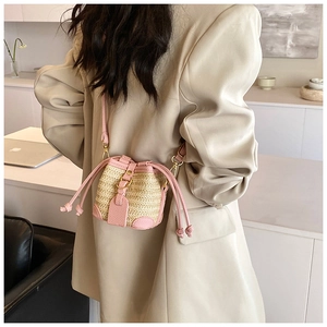 Detail of a chic straw bucket bag with pink leather trim and golden ring closure