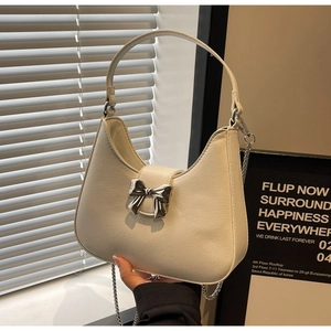 Detail of cream white half-moon bag with silver metal bow and textured leather