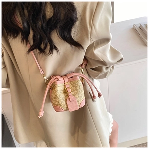 Detail of pink PU leather and woven straw bucket bag with drawstring closure worn by model
