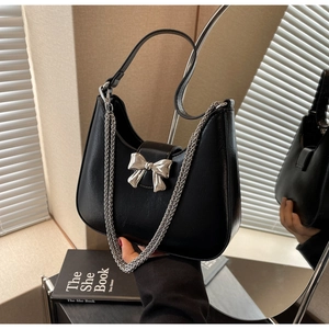 Detailed view of black patent leather crescent bag with silver bow ornament and chain strap