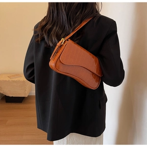 Detail view of caramel brown faux crocodile leather baguette shoulder bag on black blazer