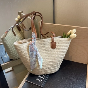Fashionable woven straw tote bag with brown leather handles and decorative blue scarf
