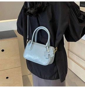 Side view of a light blue Boston handbag with gold hardware and a bow charm charm on a model