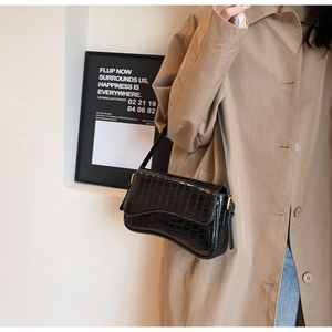 Detail shot of black crocodile embossed shoulder bag with gold metal buckle on khaki coat