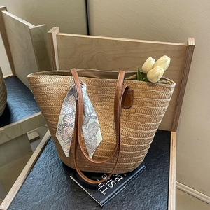 Fashionable straw woven tote bag with brown leather handles and decorative silk scarf