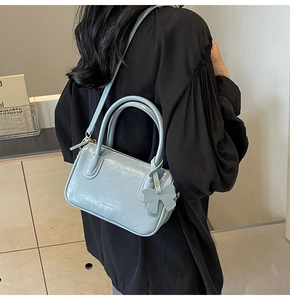 Light blue glossy PU leather handbag with bow charm shown on model in minimal room