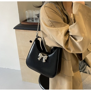 Detail of black leather underarm bag with silver bow ornament and metal chain strap