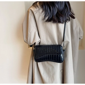 Detail shot of a black crocodile pattern shoulder bag on a model wearing a trench coat