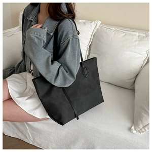 Dettaglio di una borsa tote nera minimalista su un divano bianco con outfit casual